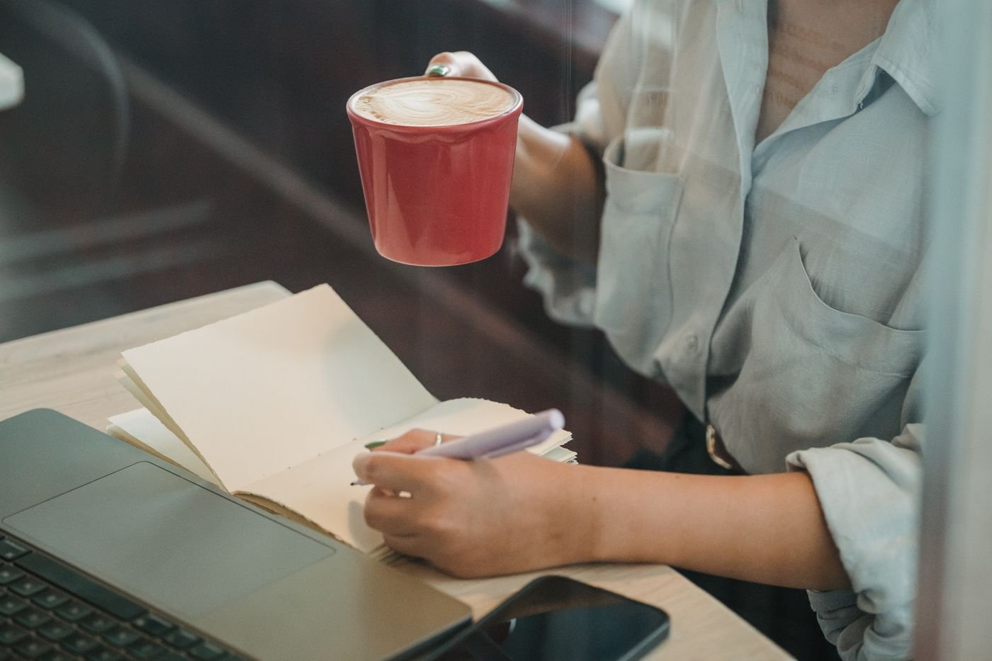 A woman writing notes in a notebook next to an open laptop