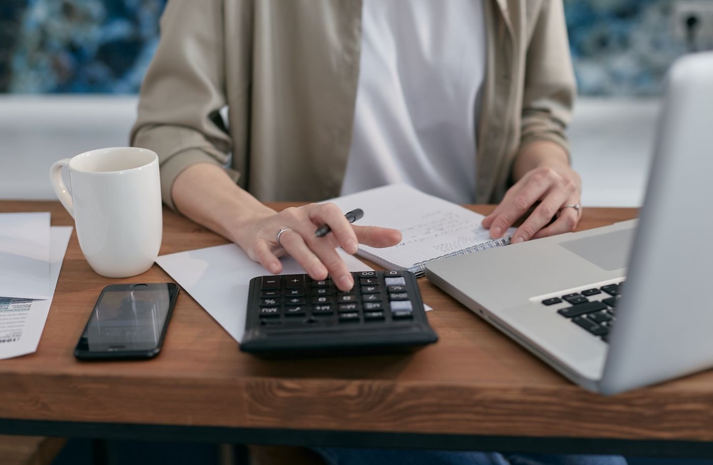 Person calculating costs with a calculator, notepad and laptop