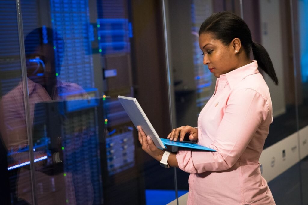An IT administrator reviewing Microsoft 365 systems on a laptop in a server room, checking patch status across Outlook and Exchange